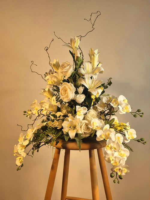 Eksklusiv vedligeholdelsesfri dekoration med hvide liljer og orkidéer, placeret stemningsfuldt på en træskammel.