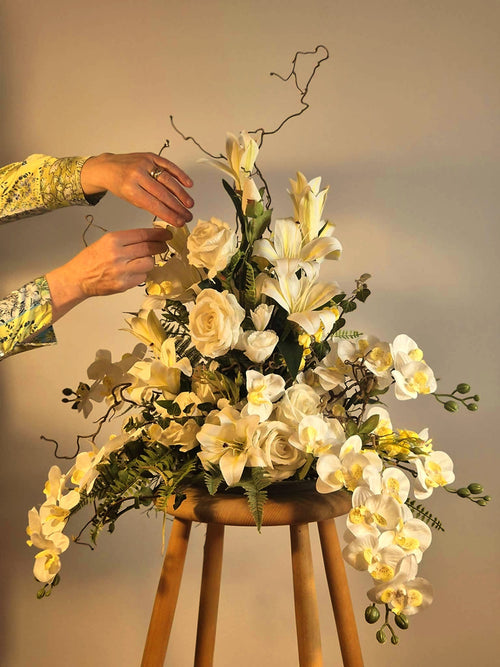 Eksklusiv hvid blomsterdekoration med liljer og orkidéer, placeret på en lys pædestal. Skaber en luksuriøs lounge stemning til erhverv.