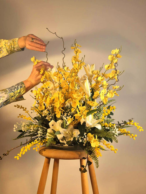 Dekoratør håndlaver en stor gul forårsdekoration af kunstige blomster på værkstedet. Skræddersyet erhvervsløsning fra Linda Blomster.