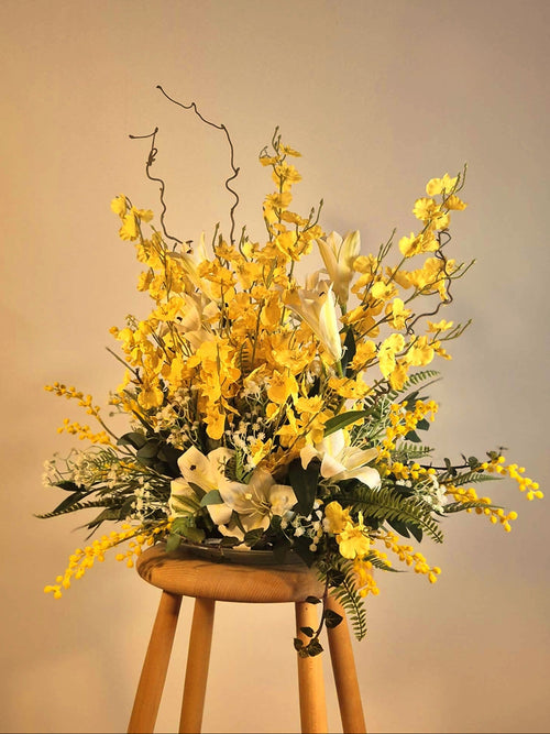 Eksklusiv gul og hvid blomsterdekoration med liljer på en pædestal. Skaber en varm og energisk lounge-stemning til erhverv.